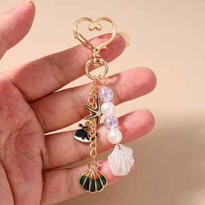 Detail of whale and starfish charms on a gold heart keychain with beads and shells