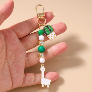 Close-up of beaded keychain featuring alpaca and cactus charms held by hand
