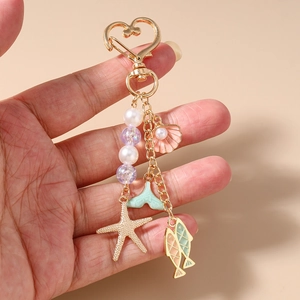 Close-up of ocean-themed keychain featuring gold starfish, shells and pearls charms