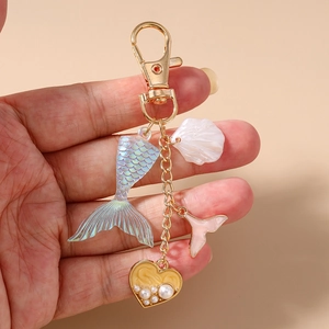 Detail of mermaid tail and heart shell keychain with pearls held by hand against pink back