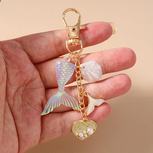 Detailed close-up of a golden keychain with shell, mermaid tail, and pearl heart charms