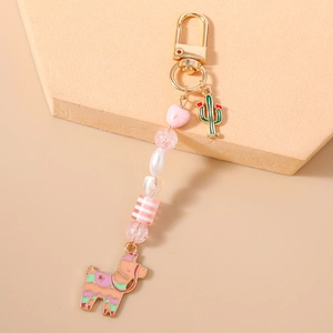 Close-up of cute alpaca keychain with cactus charm and colorful heart beads on pink stone