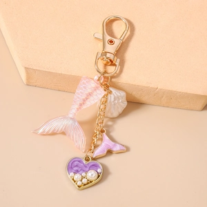 Detail of mermaid tail keychain with iridescent charms, pearl heart and gold hardware
