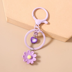 Dettaglio del portachiavi a margherita viola chiaro con ciondolo a cuore su sfondo beige