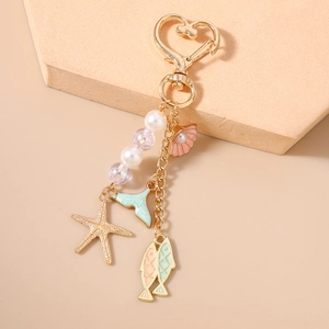 Detail of heart-shaped gold keychain with pink starfish, shell and mermaid tail charms