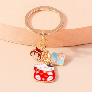 Makroaufnahme Goldener Maneki-neko Schlüsselanhänger mit Emaille-Glückstasche und Anhänger