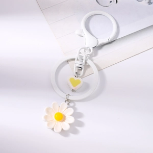 Dettaglio portachiavi con margherita bianca e cuore giallo su uno sfondo bianco pulito