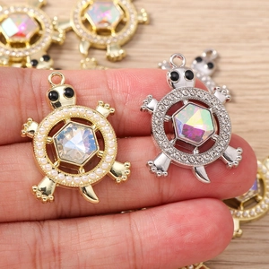 Close-up of colorful turtle pendant charms with inlaid rhinestones and pearls held by hand
