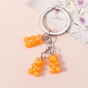 Close-up of three orange resin bears with glitter on a silver alloy keychain