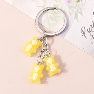 Detailed view of three yellow resin bear keychains with white skeleton prints on pink