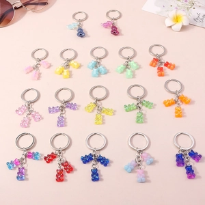 Colorful resin gummy bear keychains with silver metal rings on a soft pink background