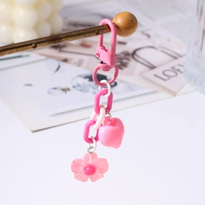 Pink heart and cherry blossom keychain displayed on a wooden stand in a cozy setting