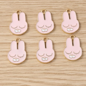 Détail de 6 pendentifs lapin en émail rose avec contour doré sur fond en bois
