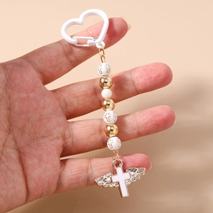 Detail of beaded keychain with gold cross prints, wing pendant and heart-shaped hook