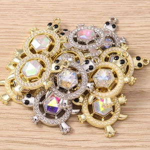 Macro detail of turtle charms with hexagonal crystal and faux pearl halo on wood
