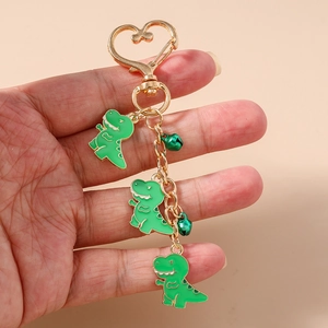 Detail of green dinosaur charms and bells on golden heart-shaped keychain held in hand