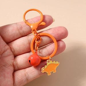 Close-up of orange dinosaur keychain with red bell and metal ring held in hand