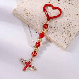 Detail of red beaded keychain with gold wings and cross on a minimalist stone background
