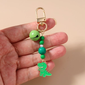 Detail of green beaded keychain with gold hook, bell, and cartoon dinosaur pendant charm