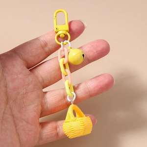 Détail d'un porte-clés panier jaune avec chaîne en plastique et clochette en main