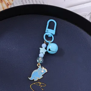 Close-up of light blue triceratops keychain with beads, bell and star charm on a tray