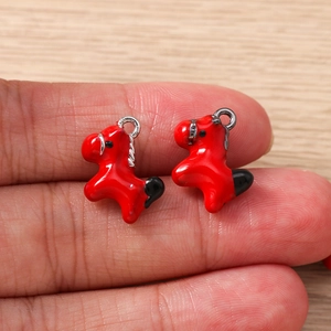 Detail showing two red enamel horse charms held on a finger for scale and size