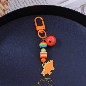 Detail of beaded dinosaur keychain with orange metal charm and colorful lacquer bell