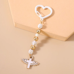Detail of beaded keychain with cross pendant and white heart clip on beige backdrop