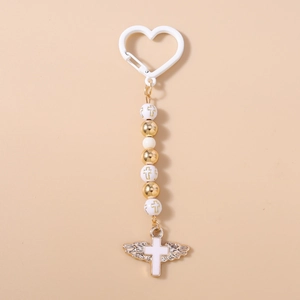 Macro detail of white beads and gold wing pendant with a cross on a vertical keychain