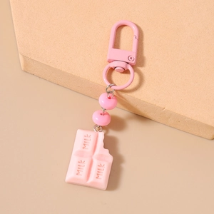 Detail of pink milk chocolate keychain with lobster clasp and resin beads on beige background