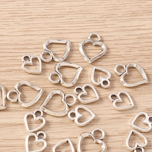 Vista macro di ciondoli a cuore cavo argentati su legno chiaro per creazione di gioielli DIY