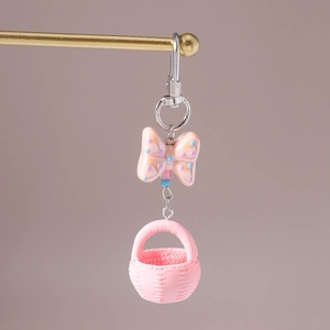 Close-up of a pink macaron-style keyring with polka dot bow and woven basket charm