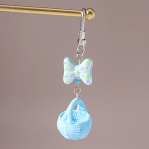 Detail view of a light blue polka dot bow and woven basket pendant on a gold keychain