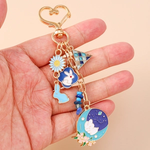 Porte-clés cœur doré avec pendentifs lapin et fleurs en émail bleu sur fond beige chaud