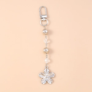 Détail d'un porte-clés fleur argentée avec perles métalliques sur fond rose tendre