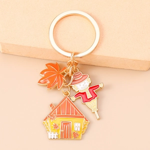 Detailed view of autumn enamel keychain with scarecrow, maple leaf and house charms