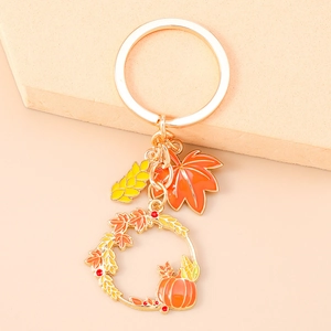 Detail view of pumpkin wreath and maple leaf keychain charms on a gold-plated ring