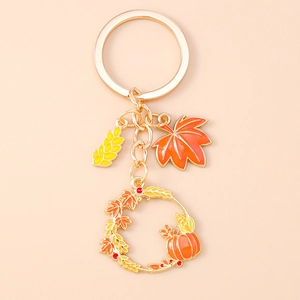 Detailed view of autumn-themed keychain featuring enamel maple leaf and pumpkin wreath charm