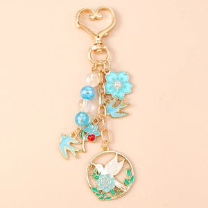 Vue détaillée de breloques florales bleues et motif d'oiseau sur porte-clés doré