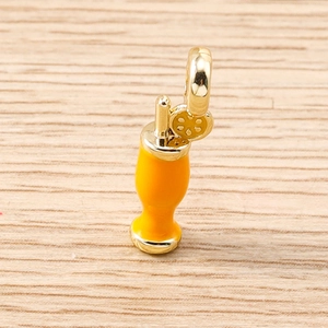 Macro detail of drink pendant with orange enamel and gold metal on wood surface
