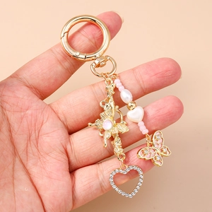 Portachiavi dorato a farfalla e cuore con perline rosa e strass tenuto in mano