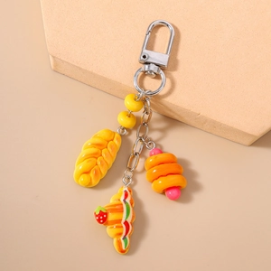 Close-up of food charm keychain with croissant and bread pendants on beige surface