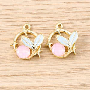 Golden round pendants with blue enamel fish tail and pink gemstone on wood surface