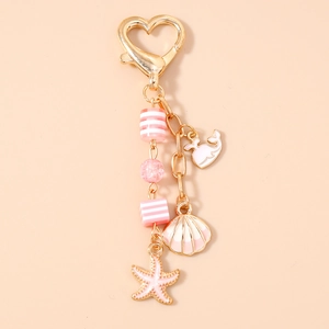 Detail of a gold heart clasp keychain with pink ocean-themed whale and shell charms