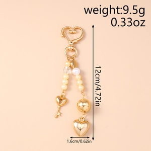 Detailed view of fashion heart keychain with white pearls and gold metal charms on a beige base