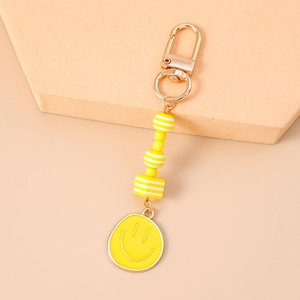 Detail of yellow beaded keychain with smiling face charm and gold clasp on beige stand