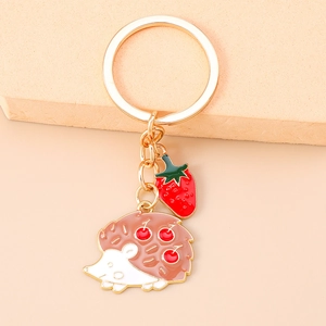 Detail of hedgehog and strawberry alloy keychain with pink and red enamel finish