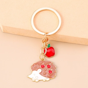 Detailed view of hedgehog keychain with red apple pendant and polished gold hardware