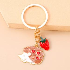 Detail of a golden keychain with cute hedgehog and strawberry charms on a pink background