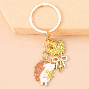 Detailed close-up of a golden alloy hedgehog keychain with enamel wheat and bow charms